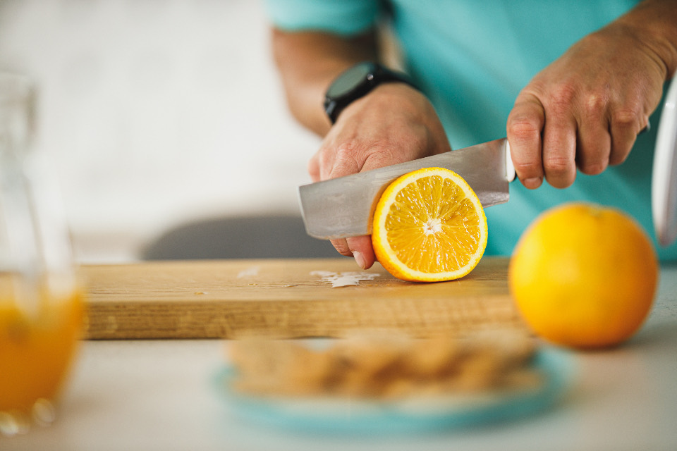 Manos cortando fruta sobre una tabla de madera en una cocina