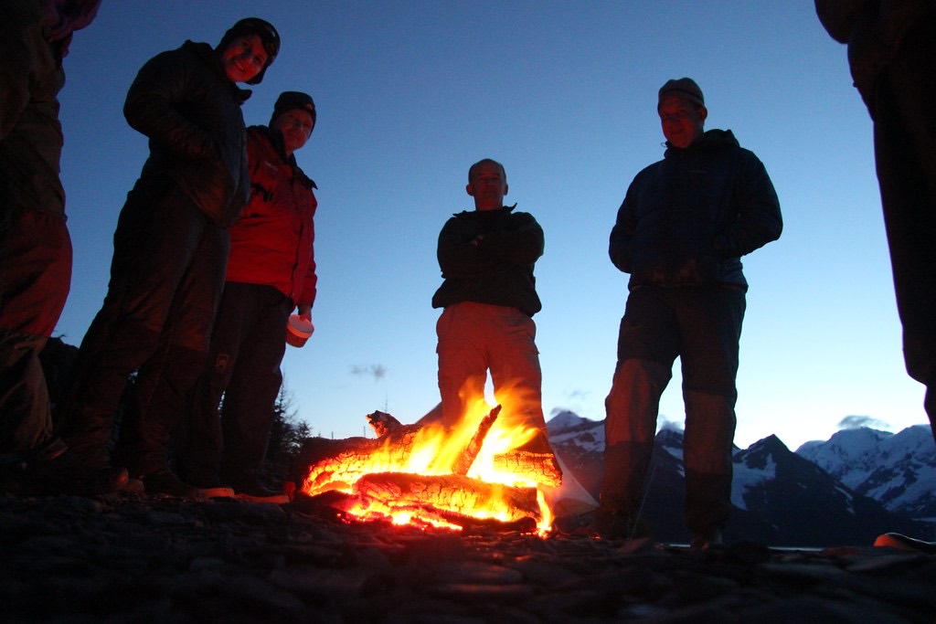 Grupo de personas en silueta junto a una fogata al atardecer